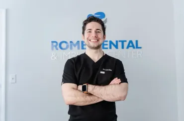 Man in black scrubs smiles with arms crossed in front of