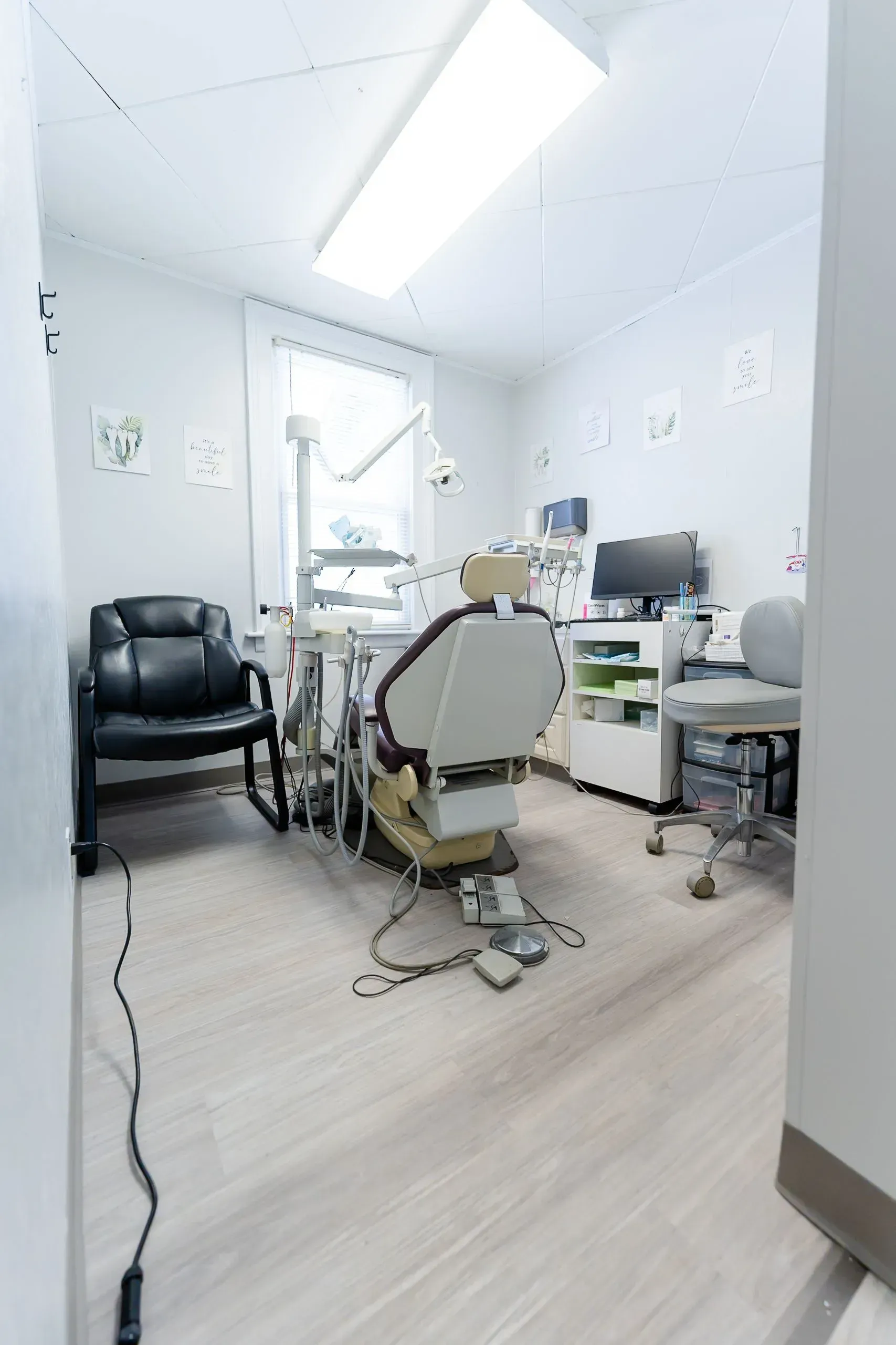 Dental office room: dental chair, equipment, X-ray images on wall, white and neutral colors.