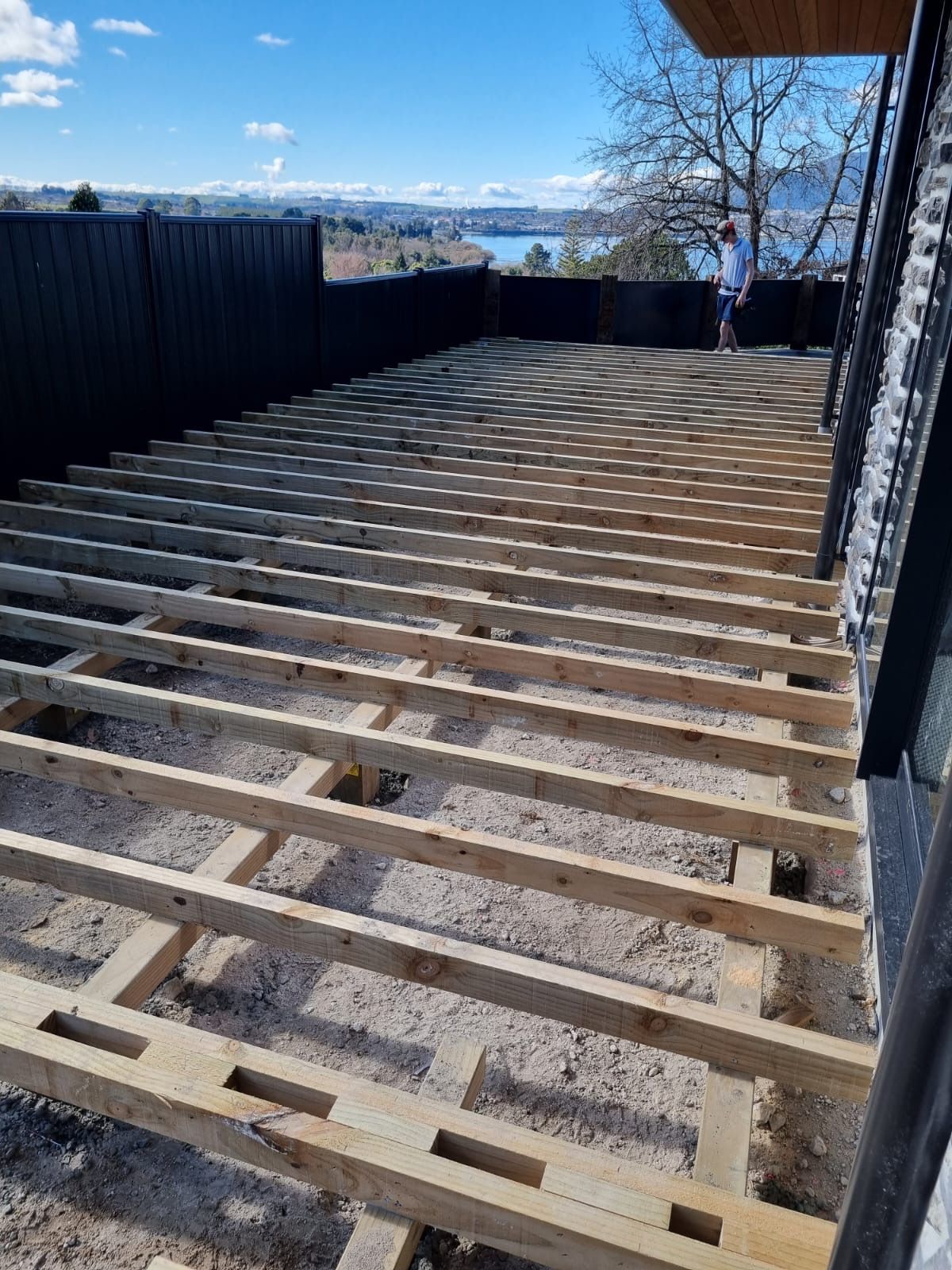 A man is standing on a wooden deck under construction.