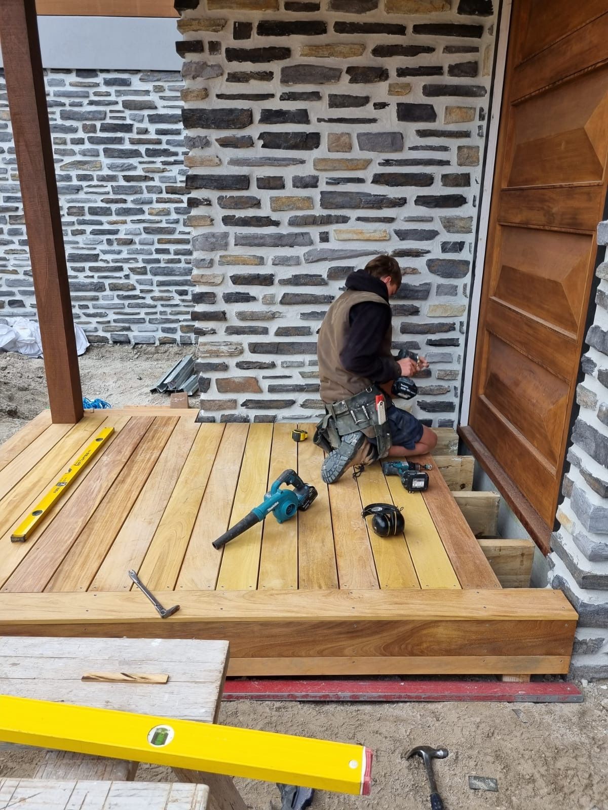 A man is working on a wooden deck in front of a brick wall.