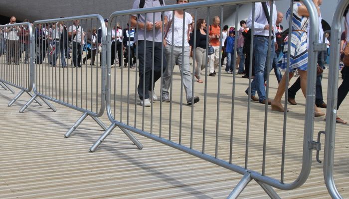A group of people are walking behind a metal barrier.