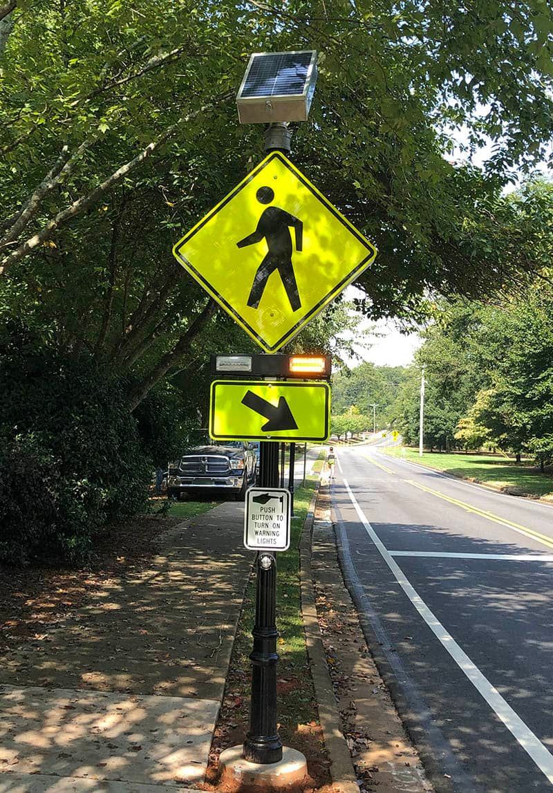 A pedestrian crossing sign is sitting on the side of a road.
