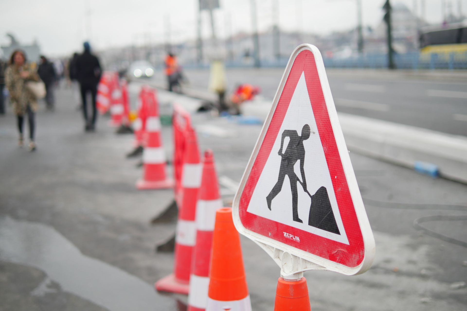 A construction sign is sitting on top of a row of orange traffic cones.