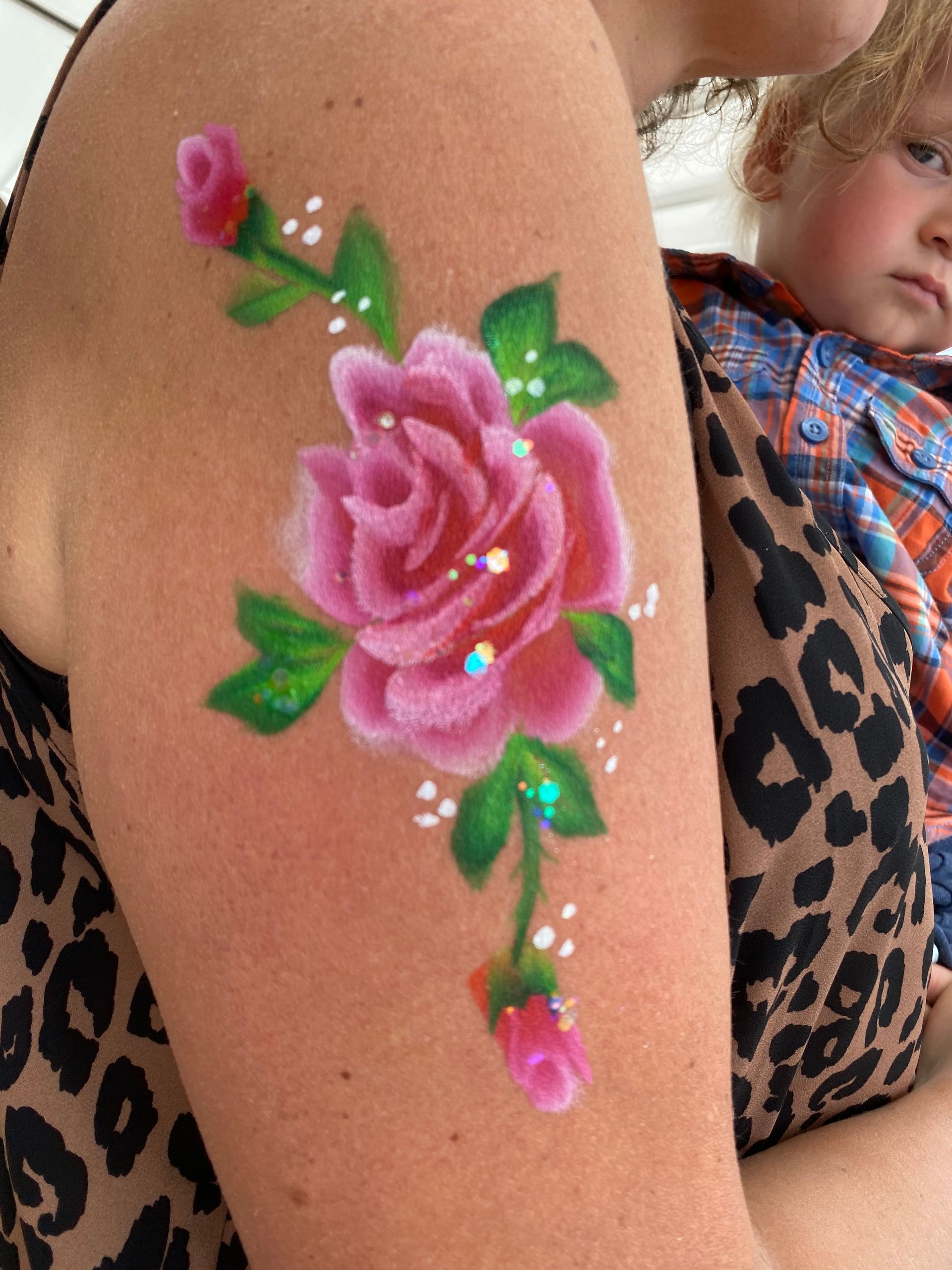 Pink rose body paint on a person's arm; a child looks on.