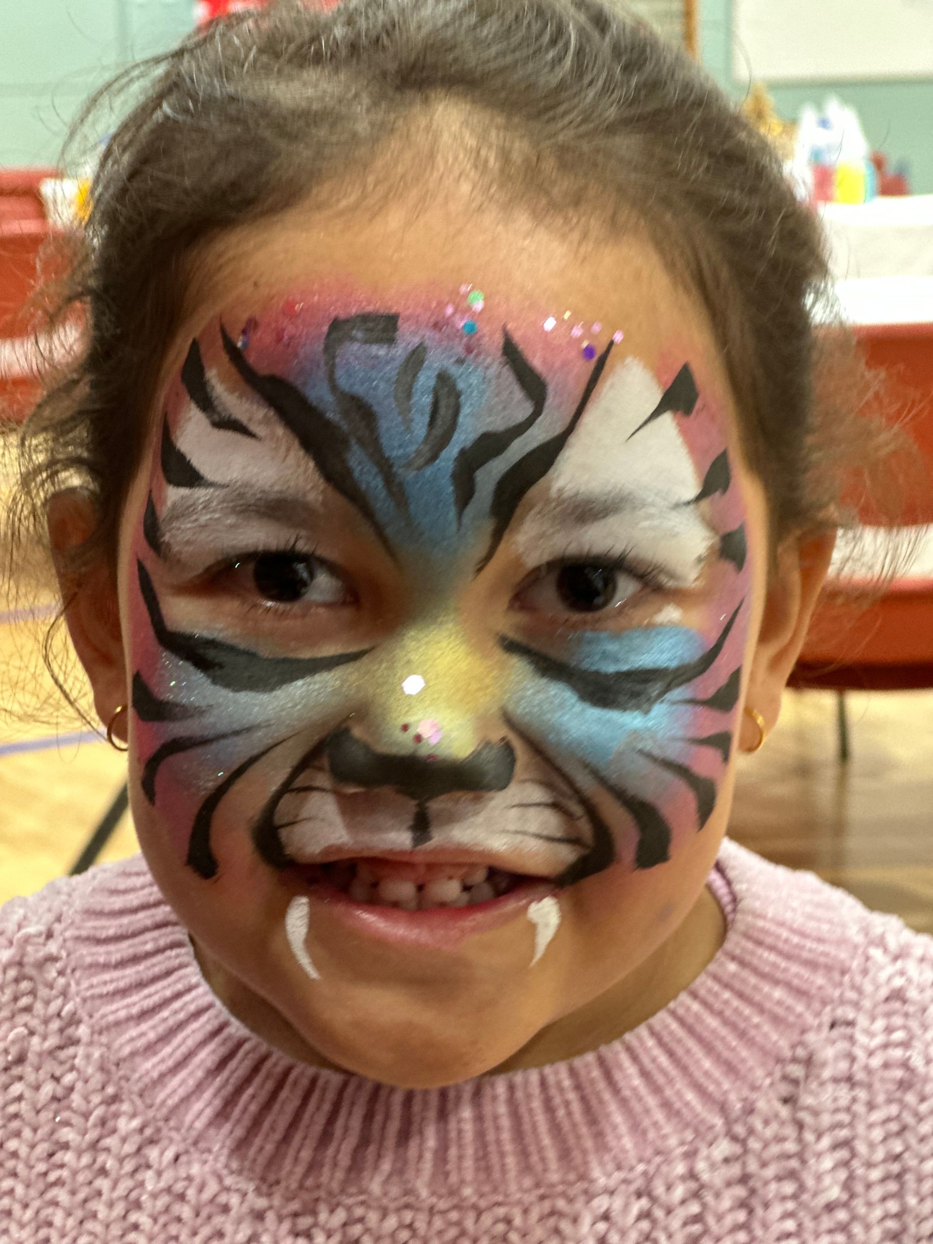 Girl with colorful tiger face paint smiles.