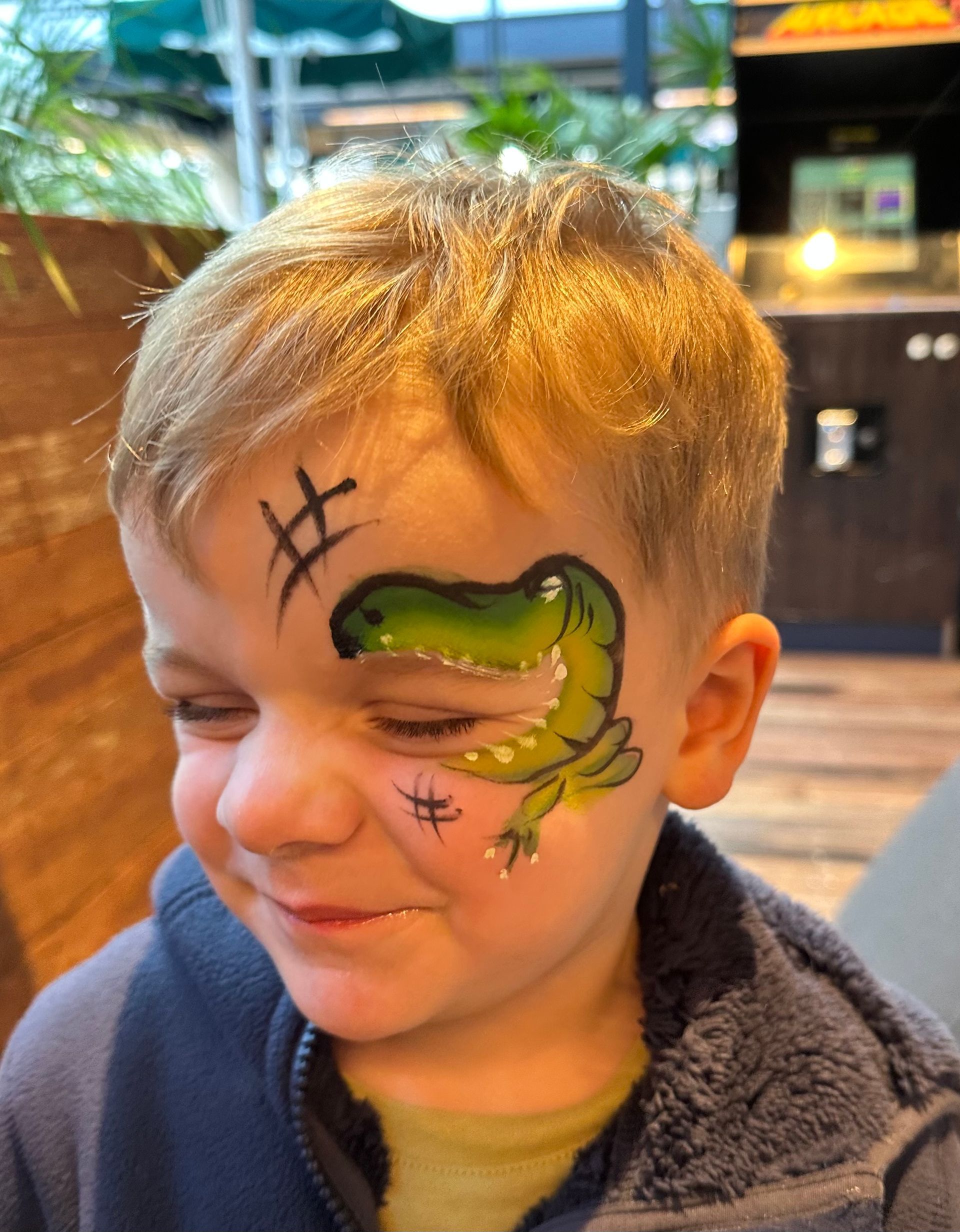 Boy with a green alligator face paint; smiling.