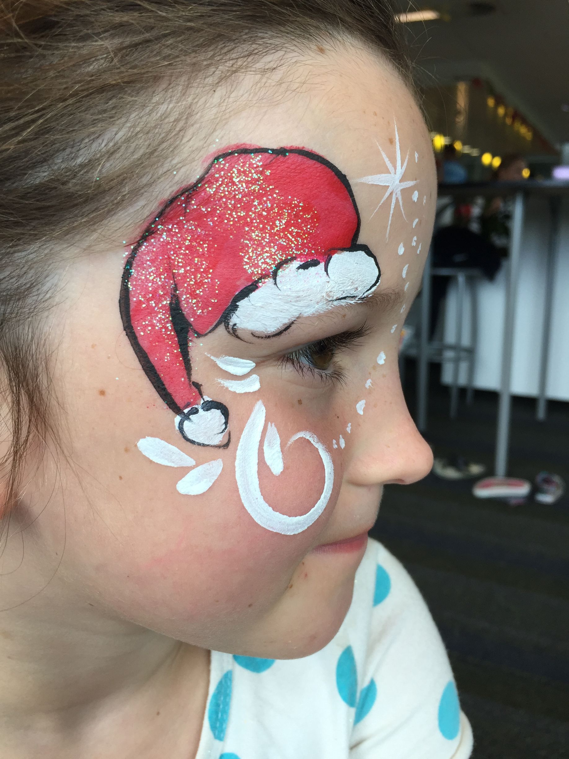 Child with Christmas face paint: Santa hat, snowflakes, and a white swirl on cheek.