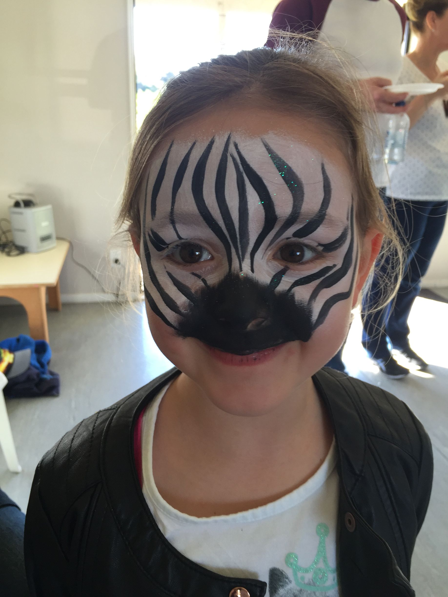 Girl with zebra face paint smiles at the camera.