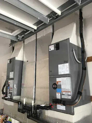 Two air conditioners are hanging from the ceiling of a garage.