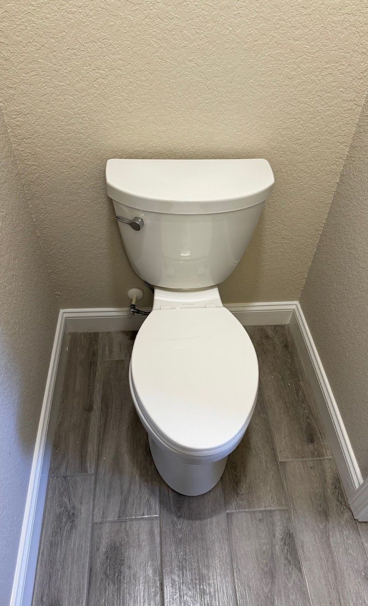 Prestige Plumbing LLC- a white toilet is sitting on a wooden floor in a bathroom.