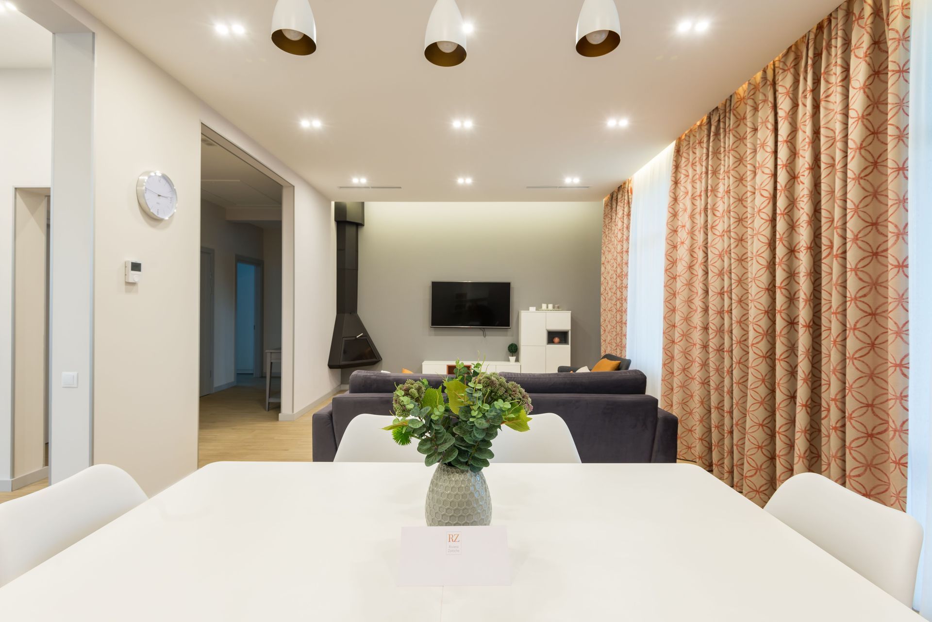 Modern living room with white dining table, gray sofa, wall TV, and patterned curtains