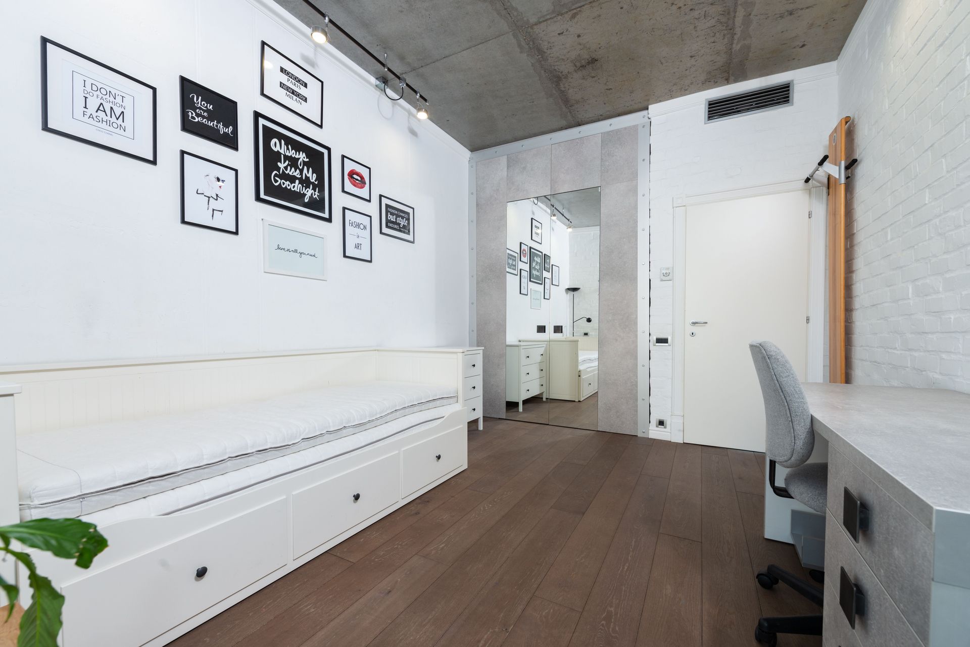 Minimalist white bedroom/office with built-in bench, framed wall art, wood floor, and desk by the window.