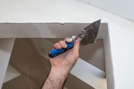 Hand using a putty knife to scrape plaster from the top corner of a wall opening
