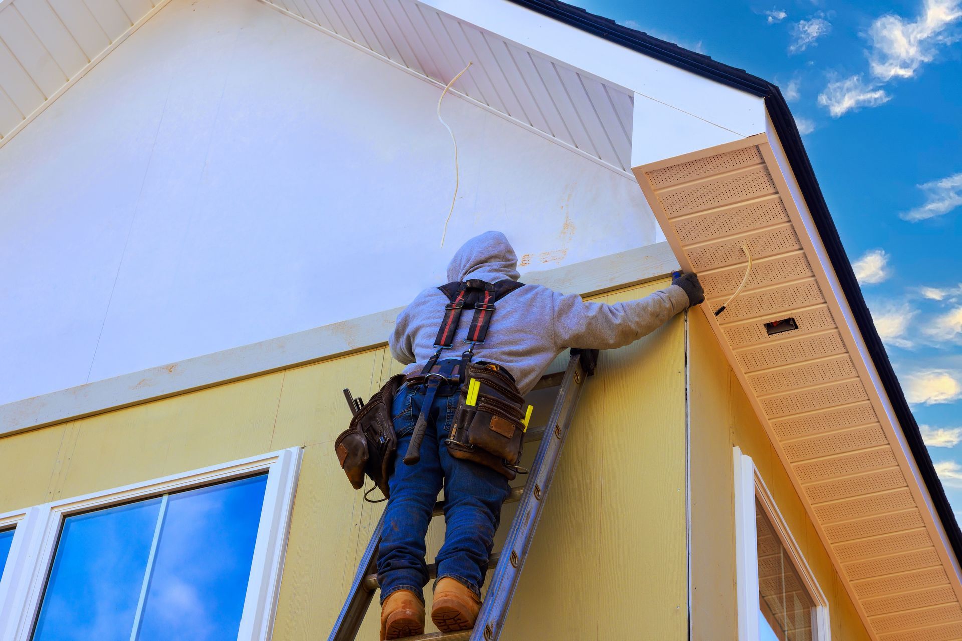 Worker on a ladder repairing the exterior trim of a house against a blue sky