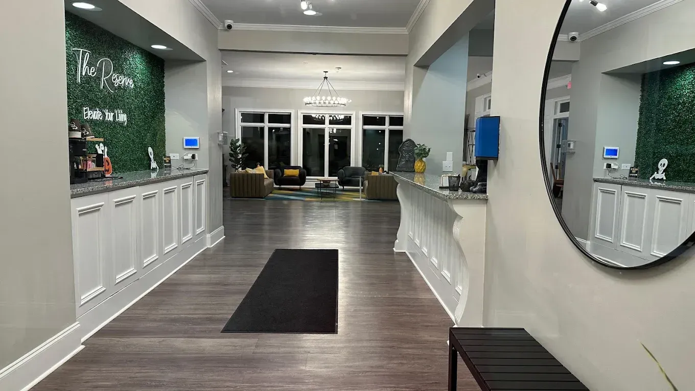 Modern lobby with white counters, round mirror, dark runner rug, and glass entrance doors.