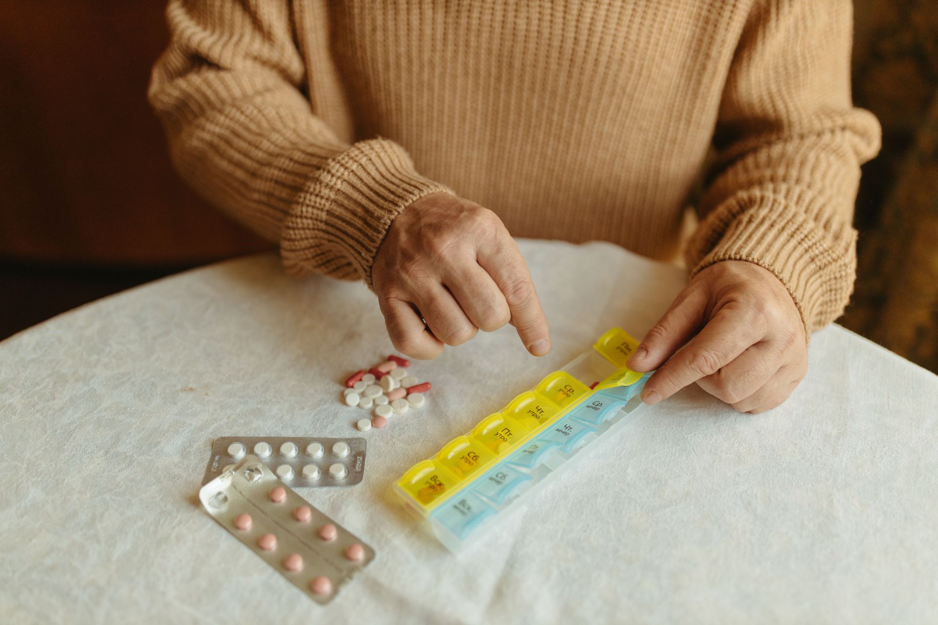 Hands placing pills into a weekly pill organizer on a table