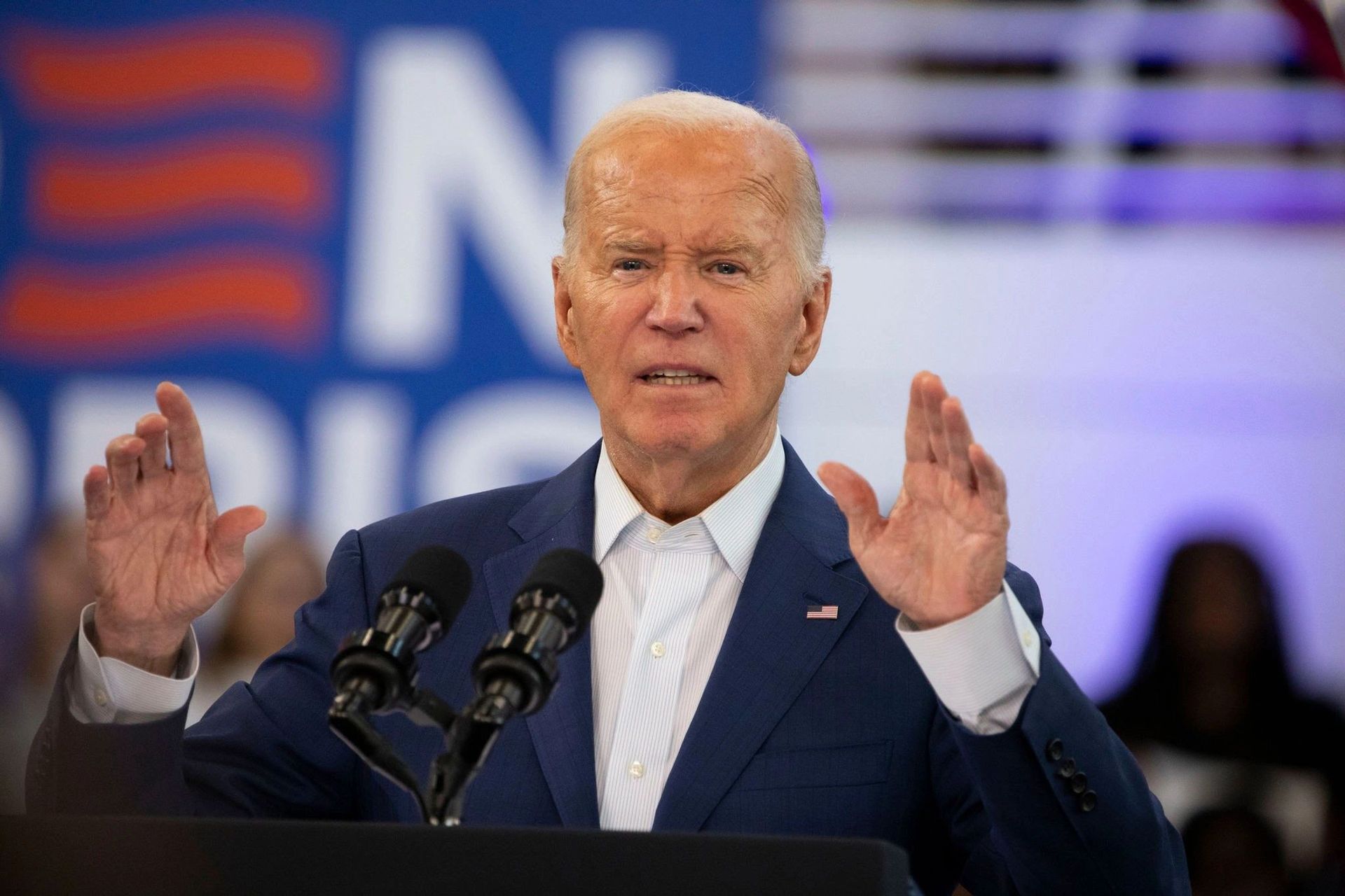A man in a suit is standing at a podium speaking into two microphones.