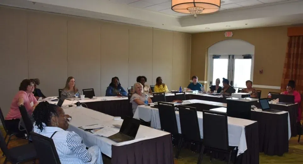 People seated around tables in a conference room during a meeting or workshop.