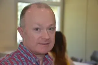 Man in red plaid shirt in an indoor office setting, looking at the camera