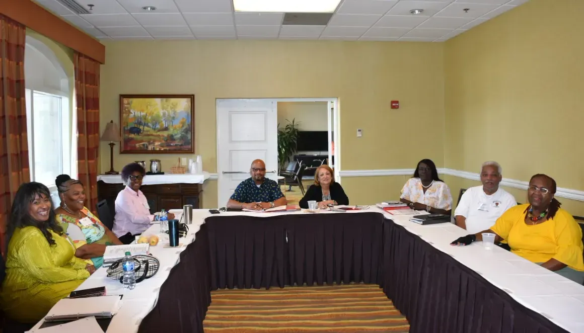 People seated around a U-shaped table in a meeting room, with papers and notebooks in front of them.
