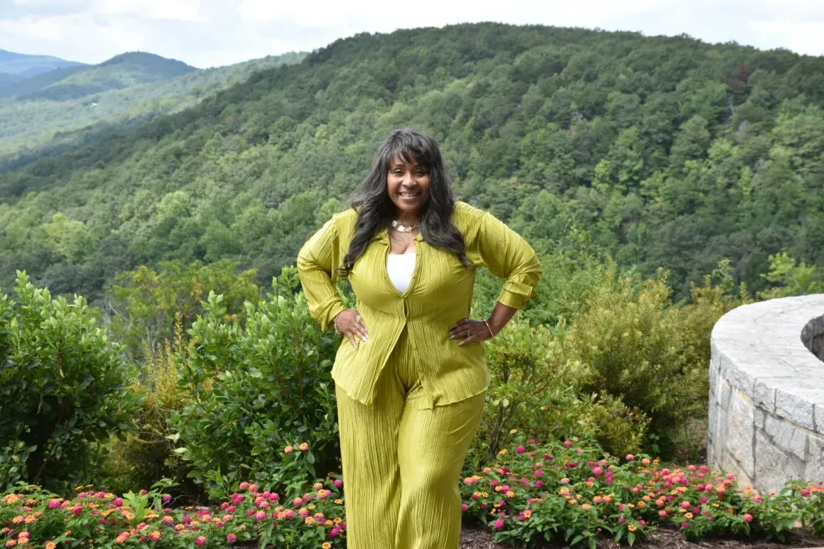 Person in a lime green outfit posing with hands on hips on a scenic mountain overlook.