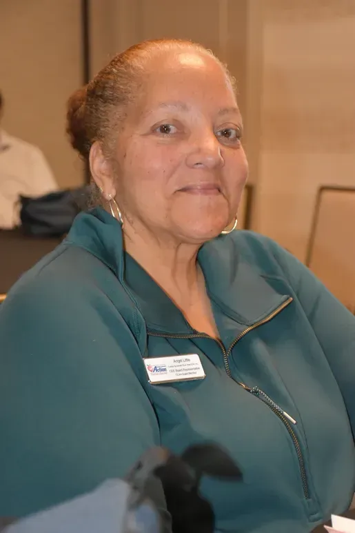 Smiling woman in a teal jacket seated indoors at a conference or event
