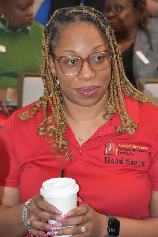 Woman in red Head Start polo holding a coffee cup in a meeting setting