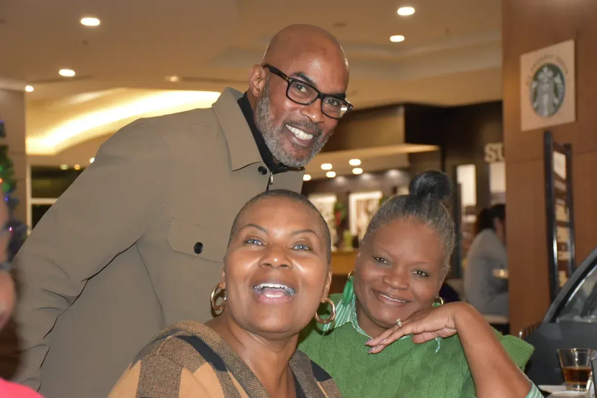 Three smiling people posing together indoors at a restaurant or event venue.