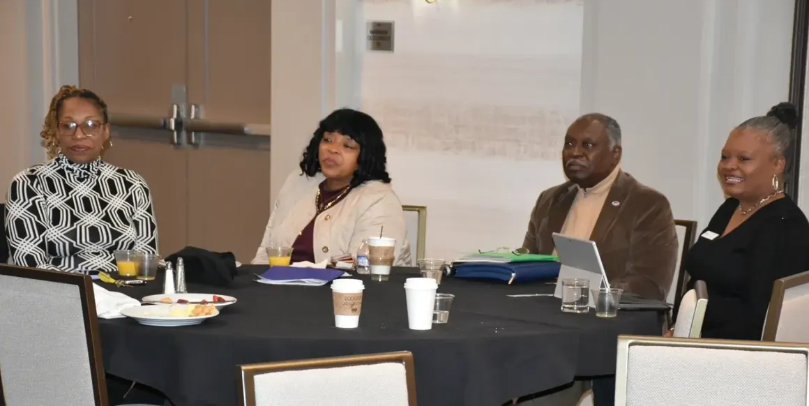 Four people seated at a conference table in a meeting room, with papers and coffee cups.