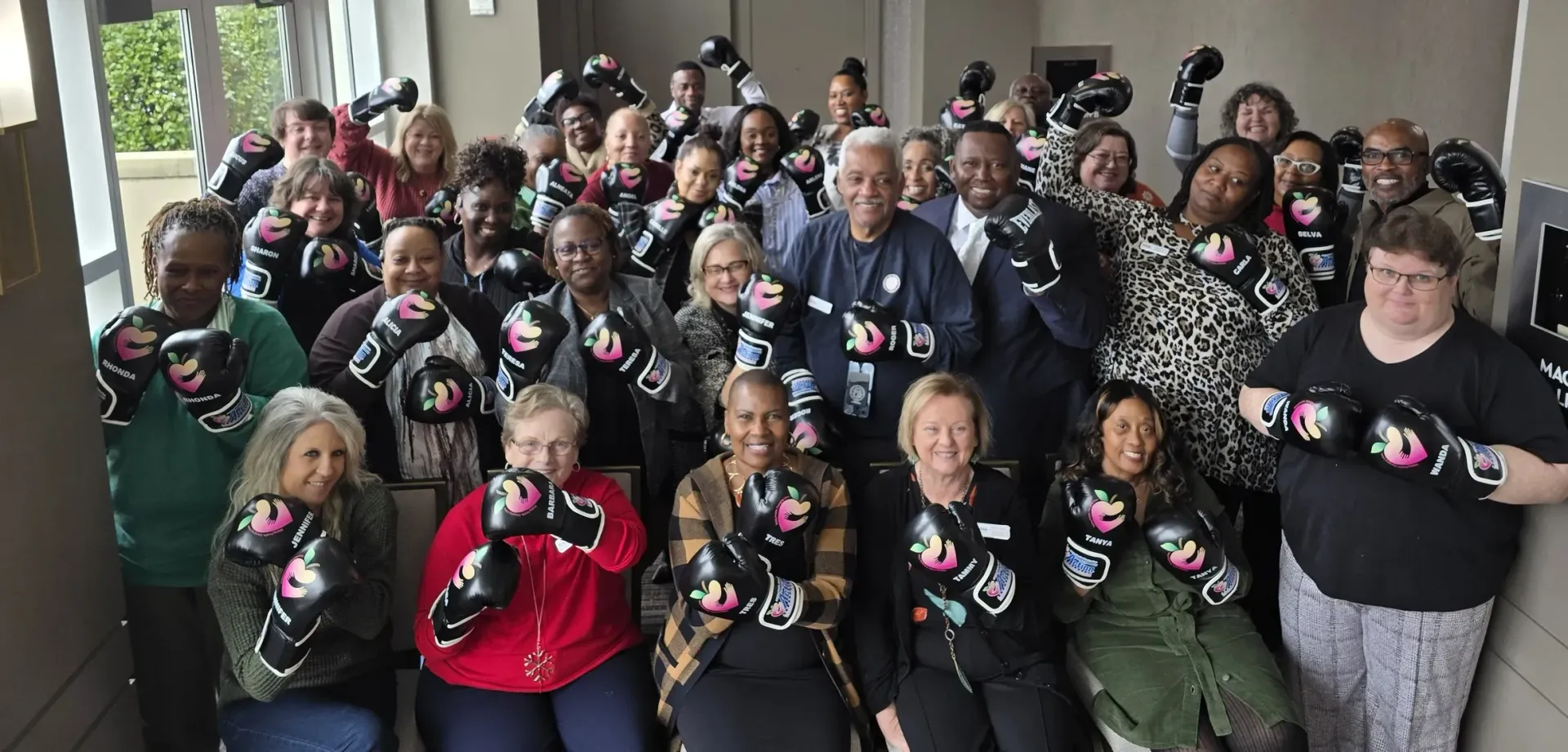 Large group posing indoors, many holding black mugs with pink hearts, smiling at the camera.