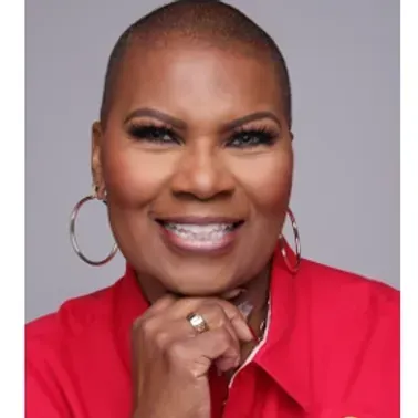 Smiling person in a red shirt with hoop earrings, resting chin on hand against a gray background