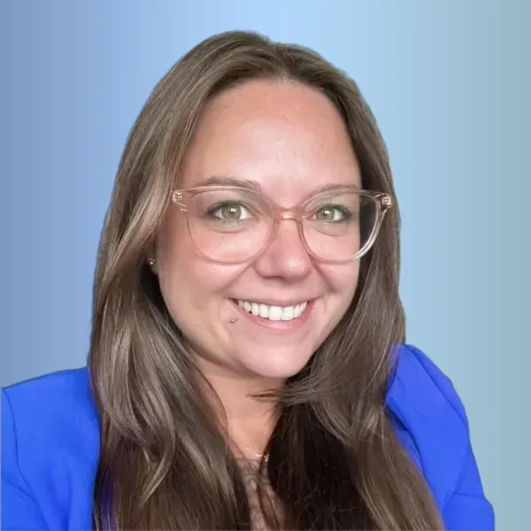 Smiling woman with glasses and long brown hair in a blue blazer on a light blue background