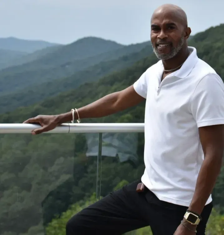 Man in white polo shirt standing on a balcony with mountain views in the background