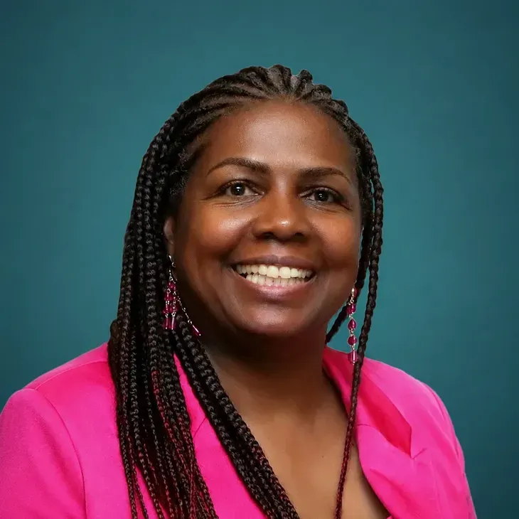 Smiling woman in a bright pink blouse against a teal background
