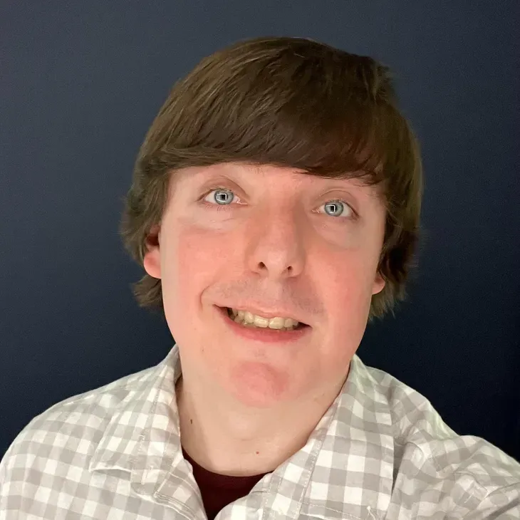 Smiling person with brown hair in a light plaid shirt against a dark blue background