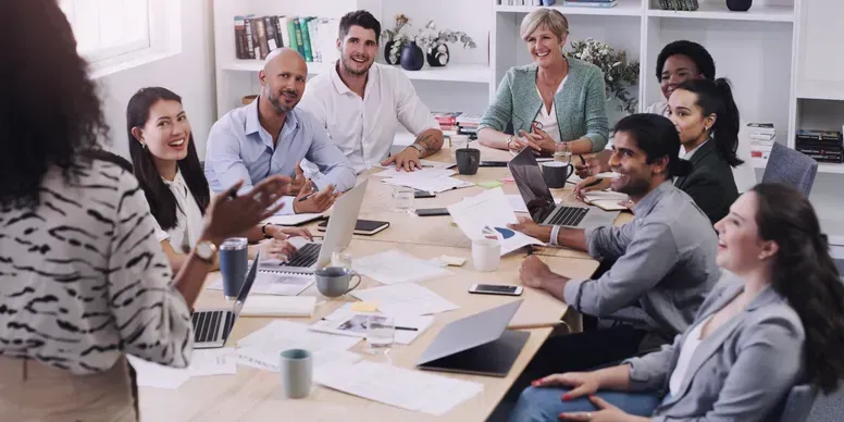 Business team meeting around a conference table with papers, laptops, and coffee cups in a bright office