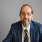 Retrato de estudio de un hombre con traje azul marino y corbata sobre un fondo gris neutro.