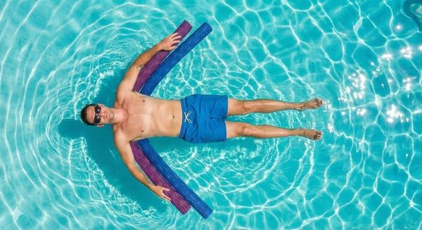 Man floating on a colorful inflatable mat in a bright blue swimming pool