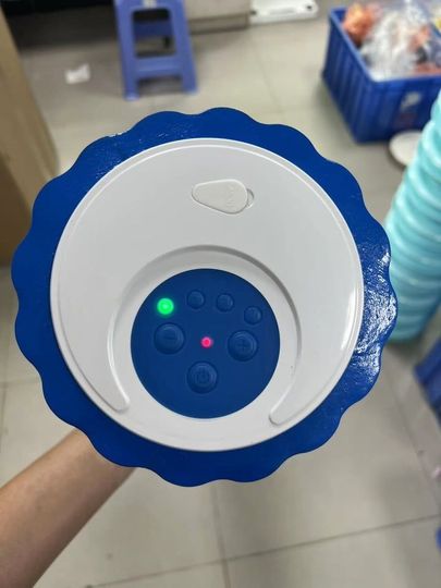 Blue-and-white round electronic device with glowing indicator lights, held in a workshop setting
