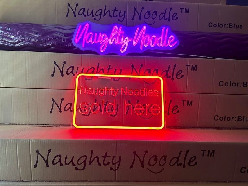 Colorful glowing “Naughty Noodle” signs, with a red neon-style “sold here” overlay in the center.