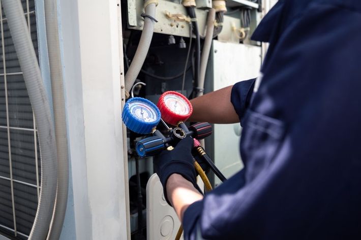 Technician using blue and red gauges to service HVAC equipment outdoors