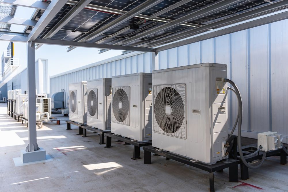 Outdoor HVAC condenser units on a rooftop under a metal canopy, with pipes and ducts attached