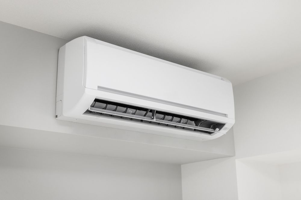 White wall-mounted air conditioner unit installed near the ceiling in a plain room