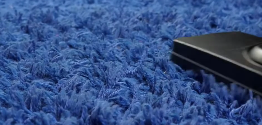 A vacuum cleaner is cleaning a blue carpet.