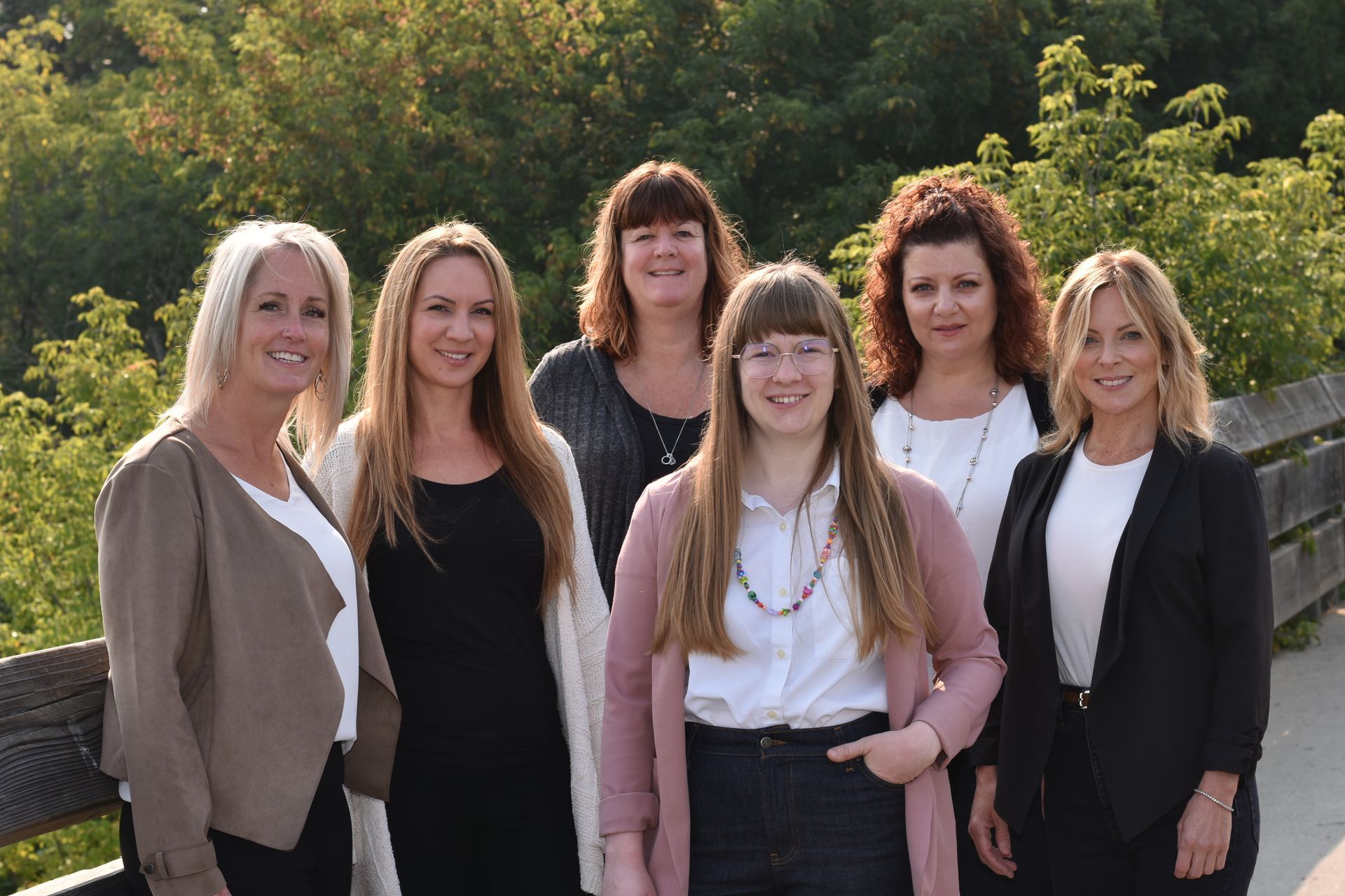 Five women standing outdoors in front of greenery, smiling at the camera.