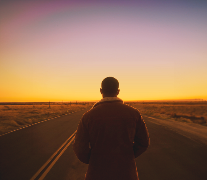 A man is walking down a road at sunset.