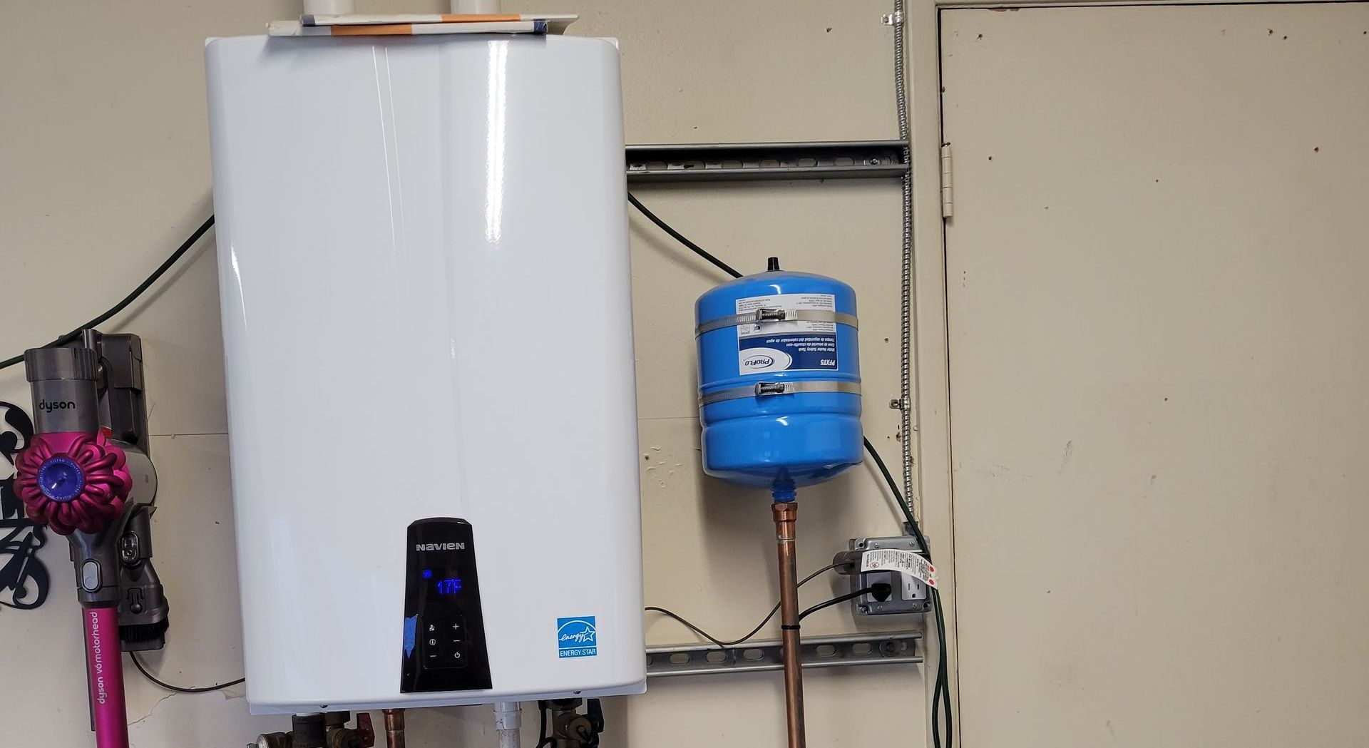 White wall-mounted water heater with a blue expansion tank and pipes in a utility room