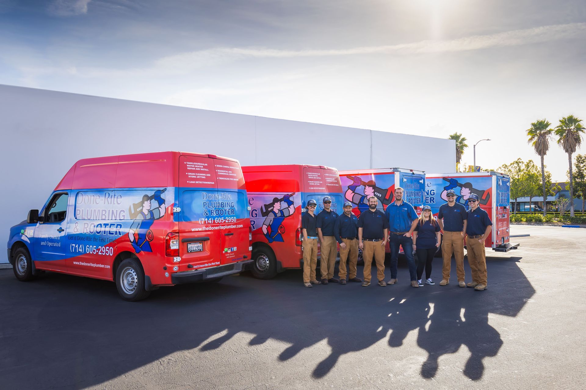 People posing with red and blue vans in a sunny parking lot with palm trees