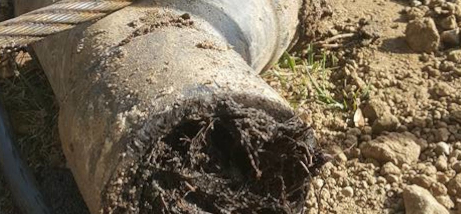 Broken concrete drain pipe with a clogged, dirty opening in a dirt trench