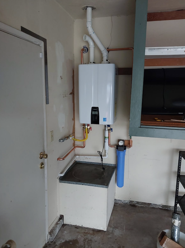 Small utility room with a wall-mounted boiler, exposed pipes, and a sink beside a door.